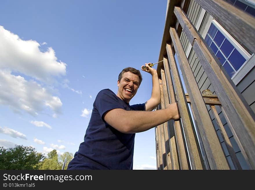 Smiling man fixing the siding on a house with a screwdriver. Horizontally framed photo. Smiling man fixing the siding on a house with a screwdriver. Horizontally framed photo.