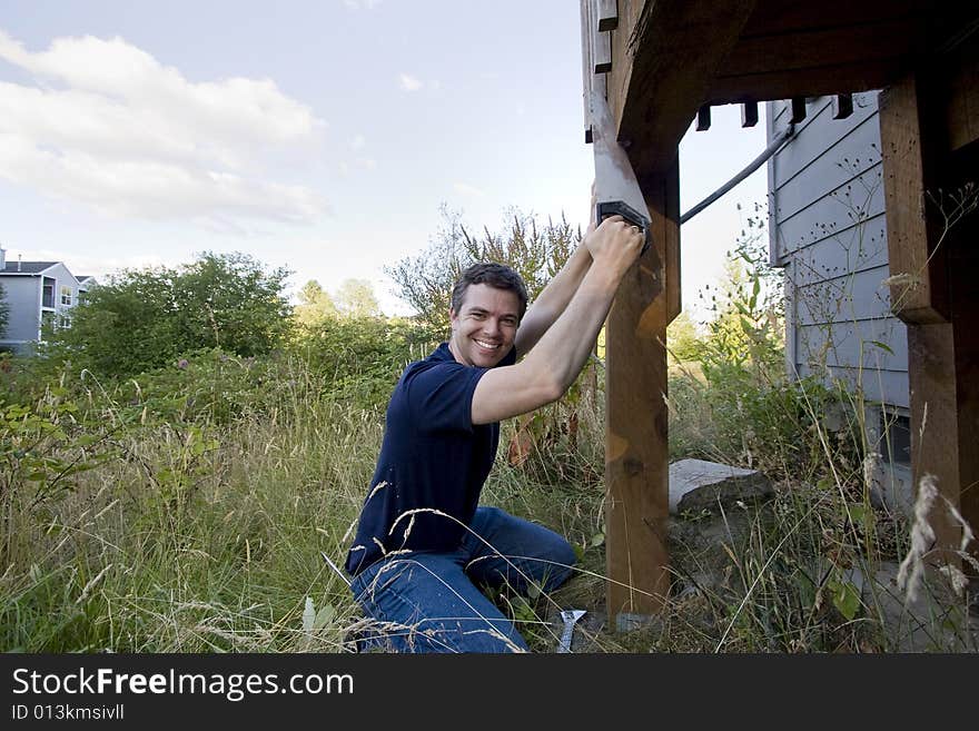 Man fixing a beam on a house with a saw. He looks happy and is smiling. Horizontally framed photo. Man fixing a beam on a house with a saw. He looks happy and is smiling. Horizontally framed photo.