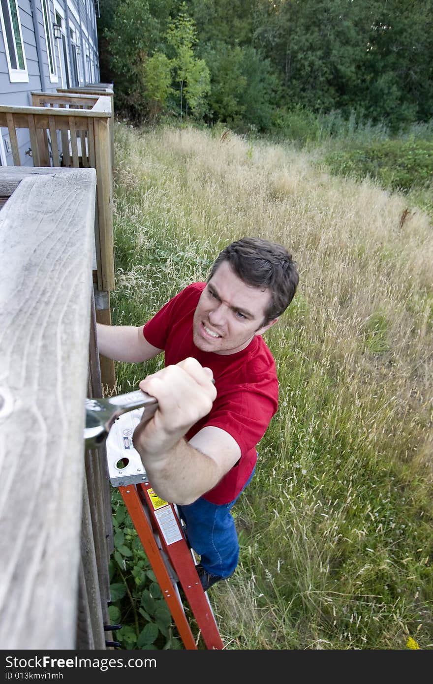 Man with a  grimace on his face standing on a ladder fixing a porch with a wrench. Vertically framed photo. Man with a  grimace on his face standing on a ladder fixing a porch with a wrench. Vertically framed photo.