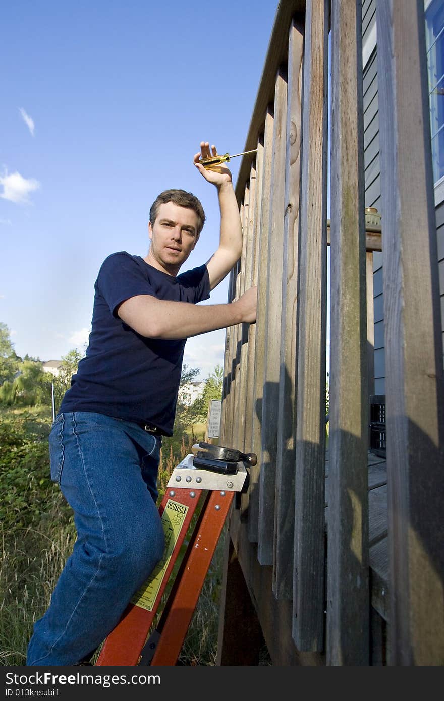 Man on a ladder repairing siding of a house with a screwdriver. Vertically framed photo. Man on a ladder repairing siding of a house with a screwdriver. Vertically framed photo.