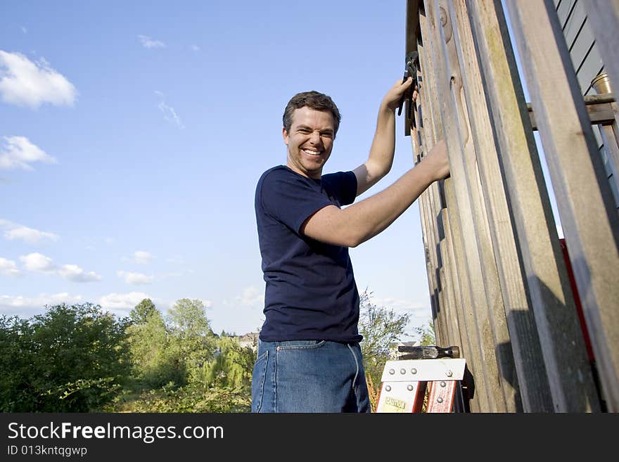 Smiling man on a ladder repairing siding of a house with a wrench. Horizontally framed photo. Smiling man on a ladder repairing siding of a house with a wrench. Horizontally framed photo.