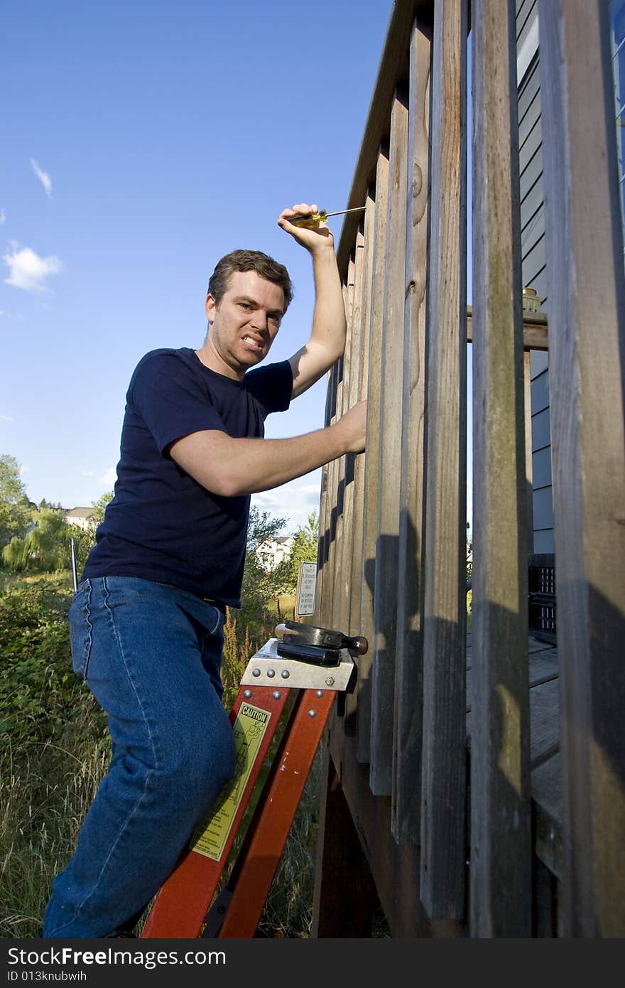 Angry man on ladder fixing the siding on a house with a screwdriver. Vertically framed photo. Angry man on ladder fixing the siding on a house with a screwdriver. Vertically framed photo.