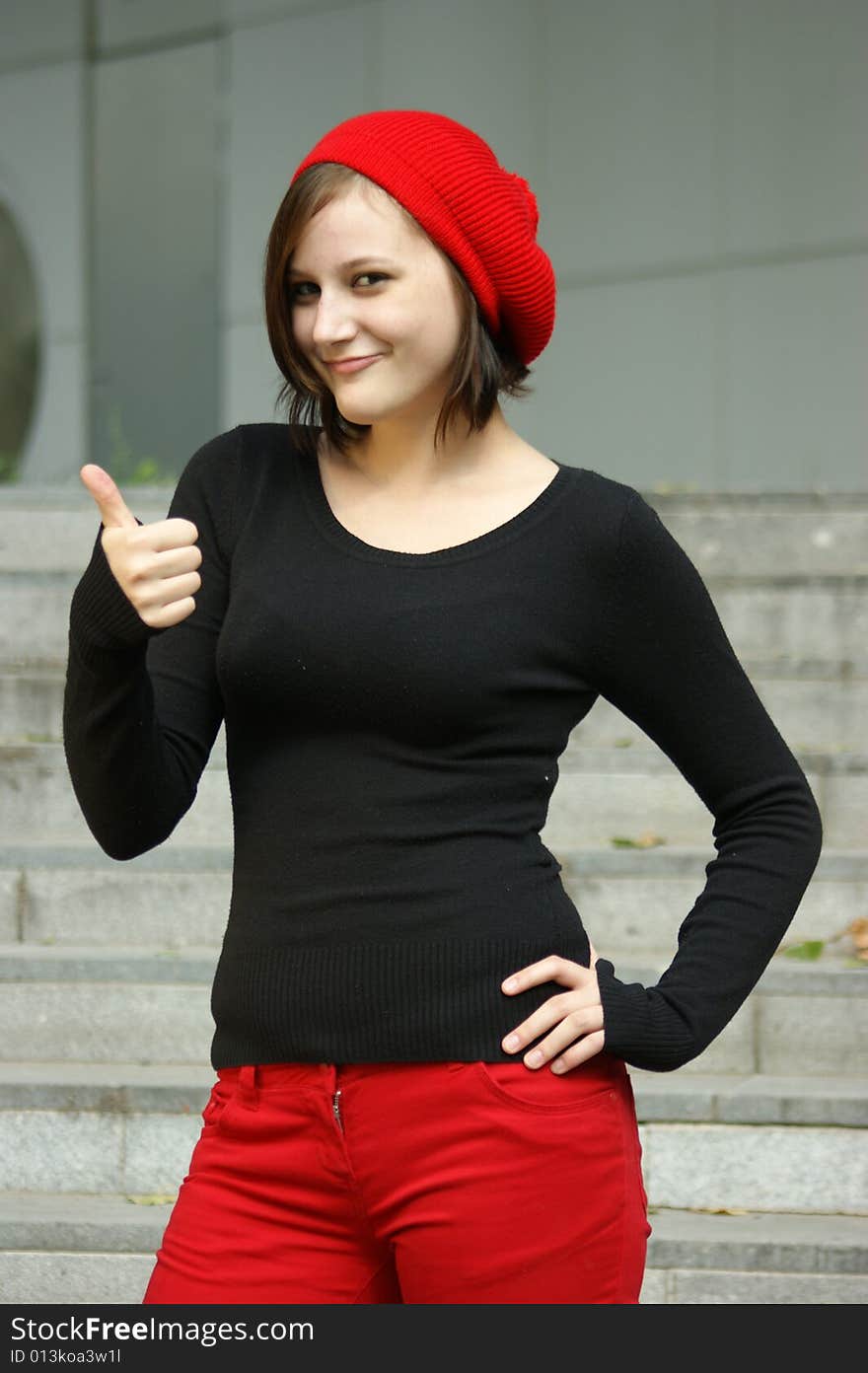 A young girl with red cap stretches thumb in the air. A young girl with red cap stretches thumb in the air