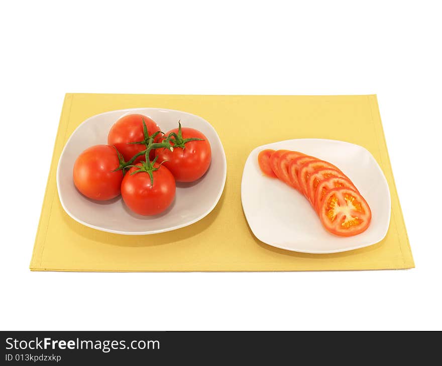 Whole and sliced tomato on white plates on yellow place mat. Whole and sliced tomato on white plates on yellow place mat