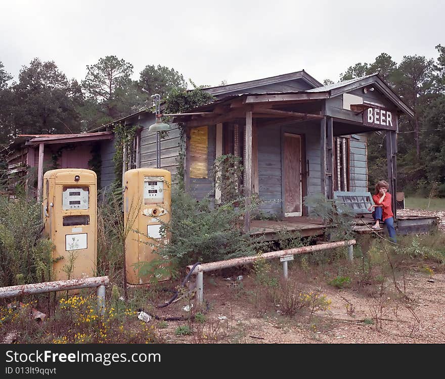 Old Gas Station with sad woman sitting on the porch steps with two yellow gas pumps out front. Old Gas Station with sad woman sitting on the porch steps with two yellow gas pumps out front.