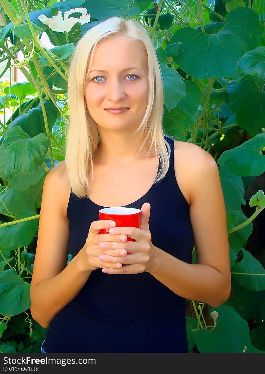 Young beautiful woman with a cup in the morning in a summer garden. Young beautiful woman with a cup in the morning in a summer garden.