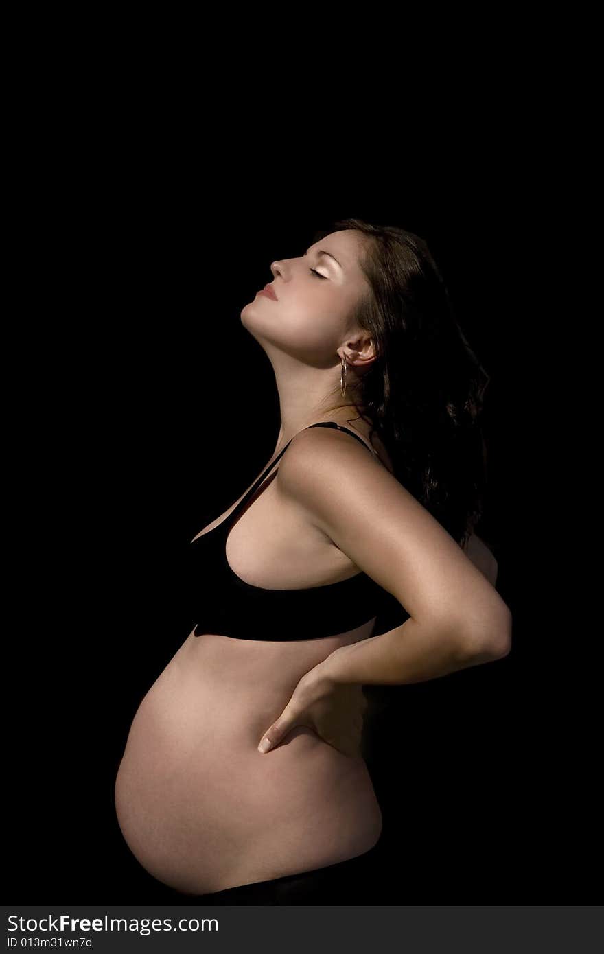 Pregnant female with a burnished gold and copper tint to her skin wearing a black bra and pants, over black background. Pregnant female with a burnished gold and copper tint to her skin wearing a black bra and pants, over black background.