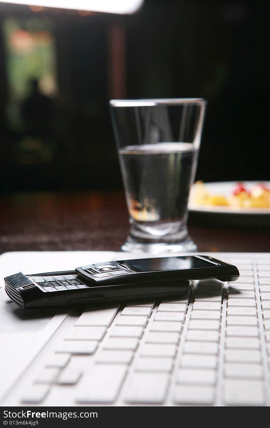 Mobile phone on white pc keyboard with cup of water