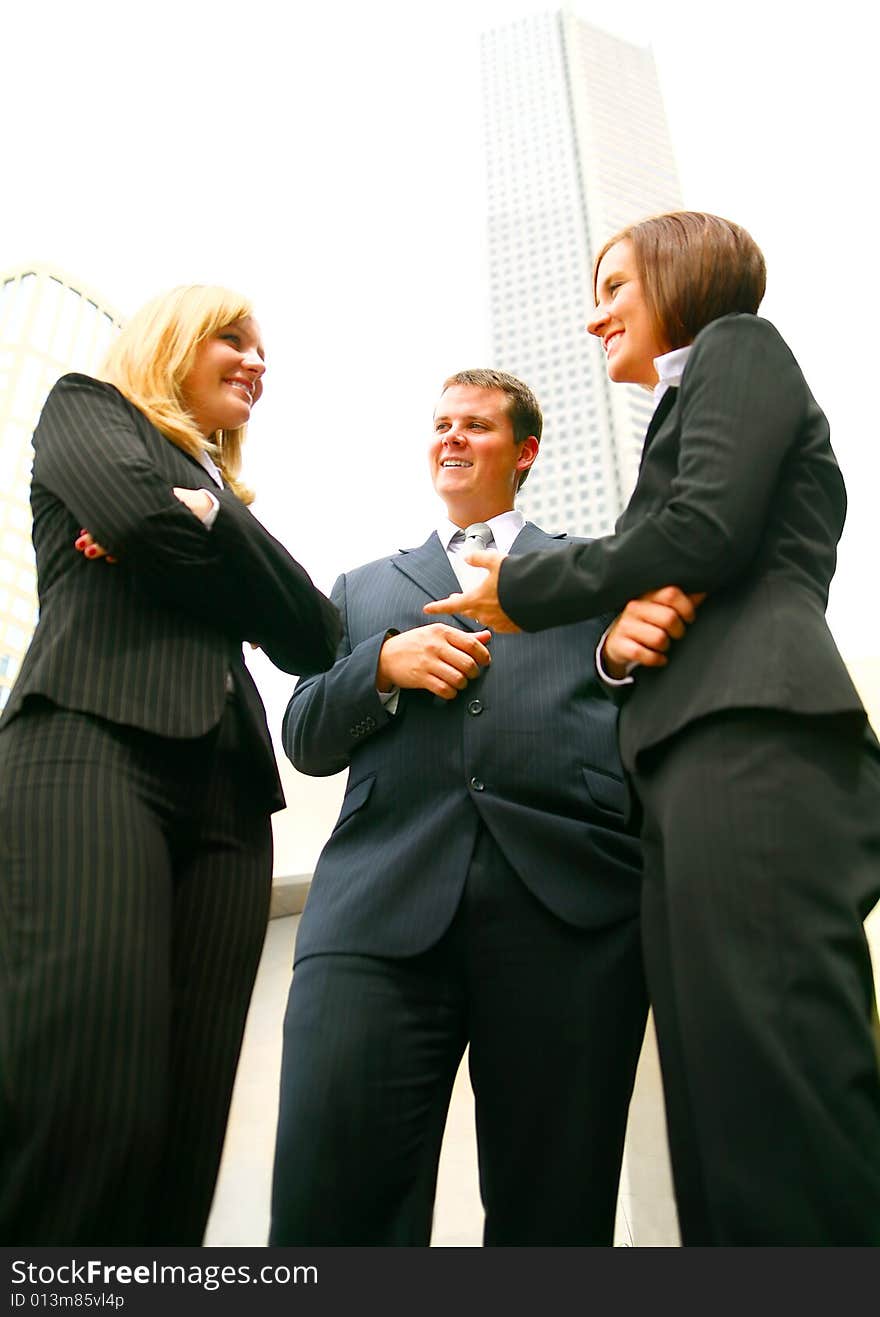 Three business people discuss as a team outdoor with tall downtown building on the background. Three business people discuss as a team outdoor with tall downtown building on the background