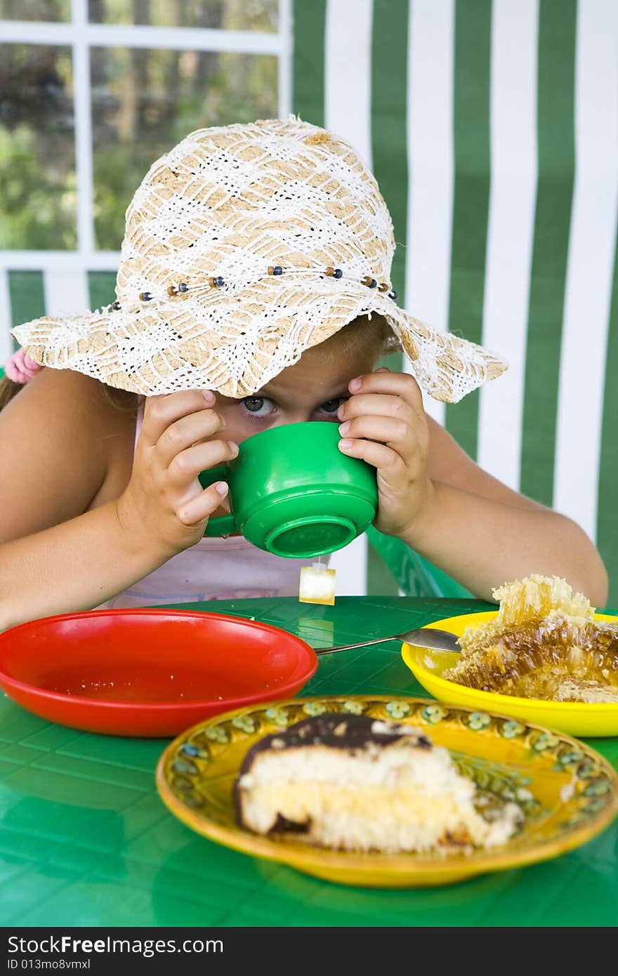 Little girl in big hat eats sweets and drinks tea. Little girl in big hat eats sweets and drinks tea