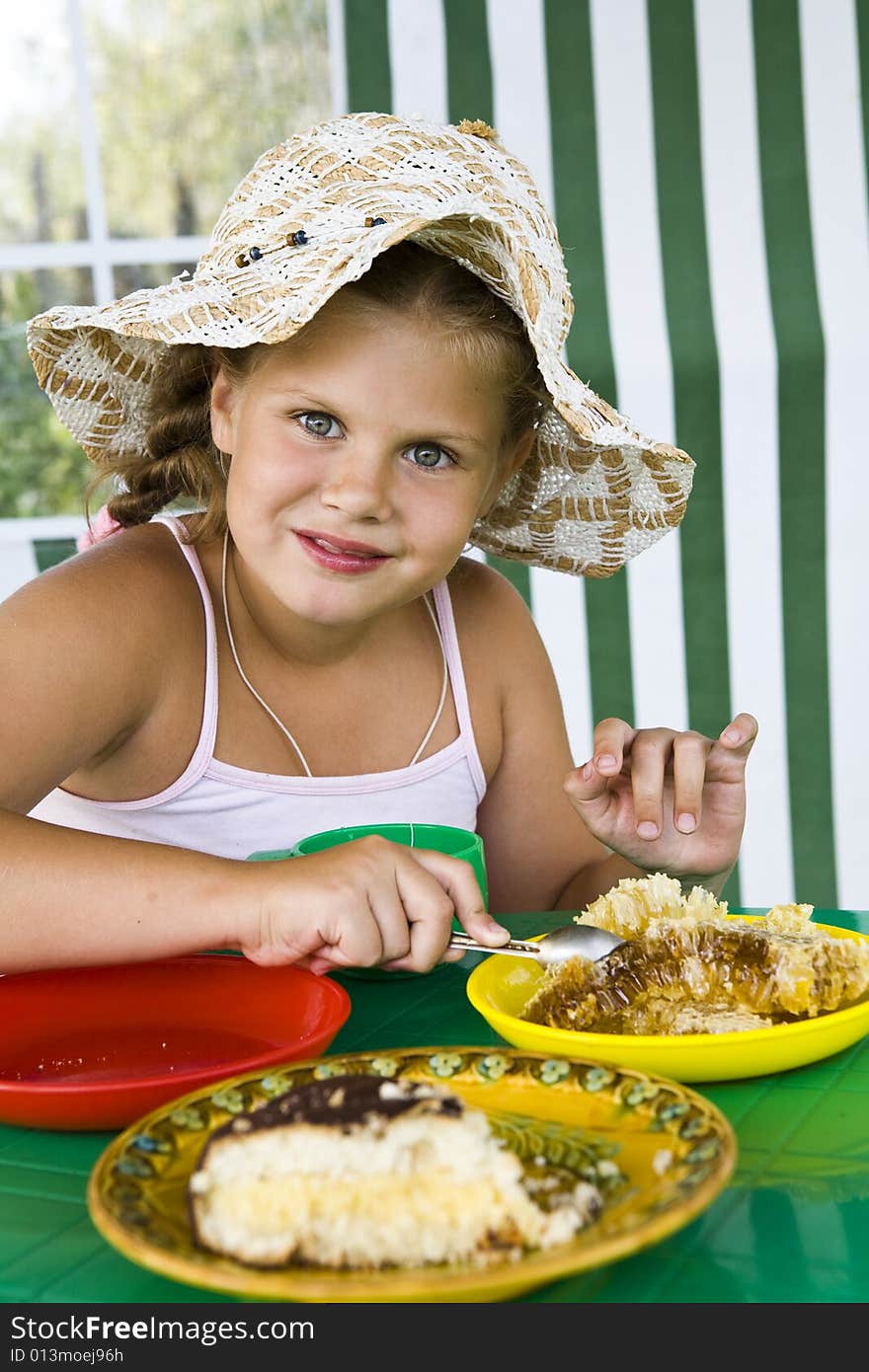 Little girl in big hat eats sweets and drinks tea