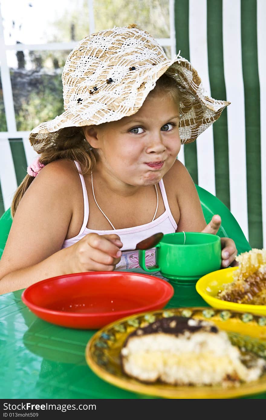 Little girl in big hat eats sweets and drinks tea. Little girl in big hat eats sweets and drinks tea