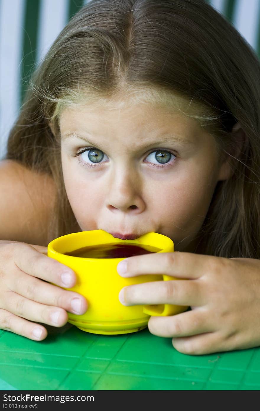 Little blond girl with yellow cup of tea in her hands