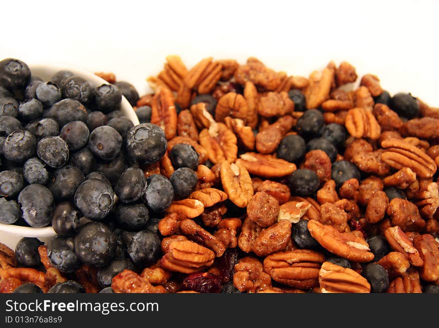 Bluberries, pecans and praline spilled from a white bowl onto a white background. Bluberries, pecans and praline spilled from a white bowl onto a white background