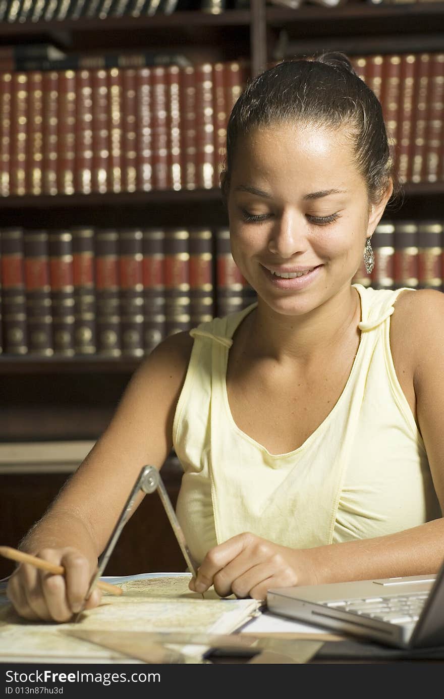 Student smiles as she works with a protractor in an office surrounded by books. Vertically framed photo. Student smiles as she works with a protractor in an office surrounded by books. Vertically framed photo.