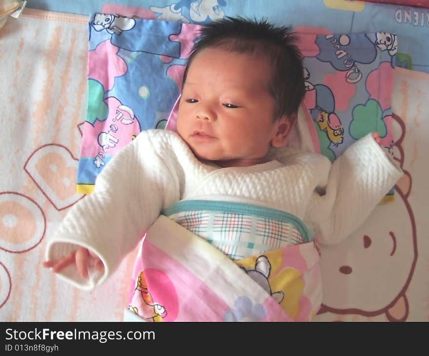 A Chinese infant is waving her hand on the bed. A Chinese infant is waving her hand on the bed