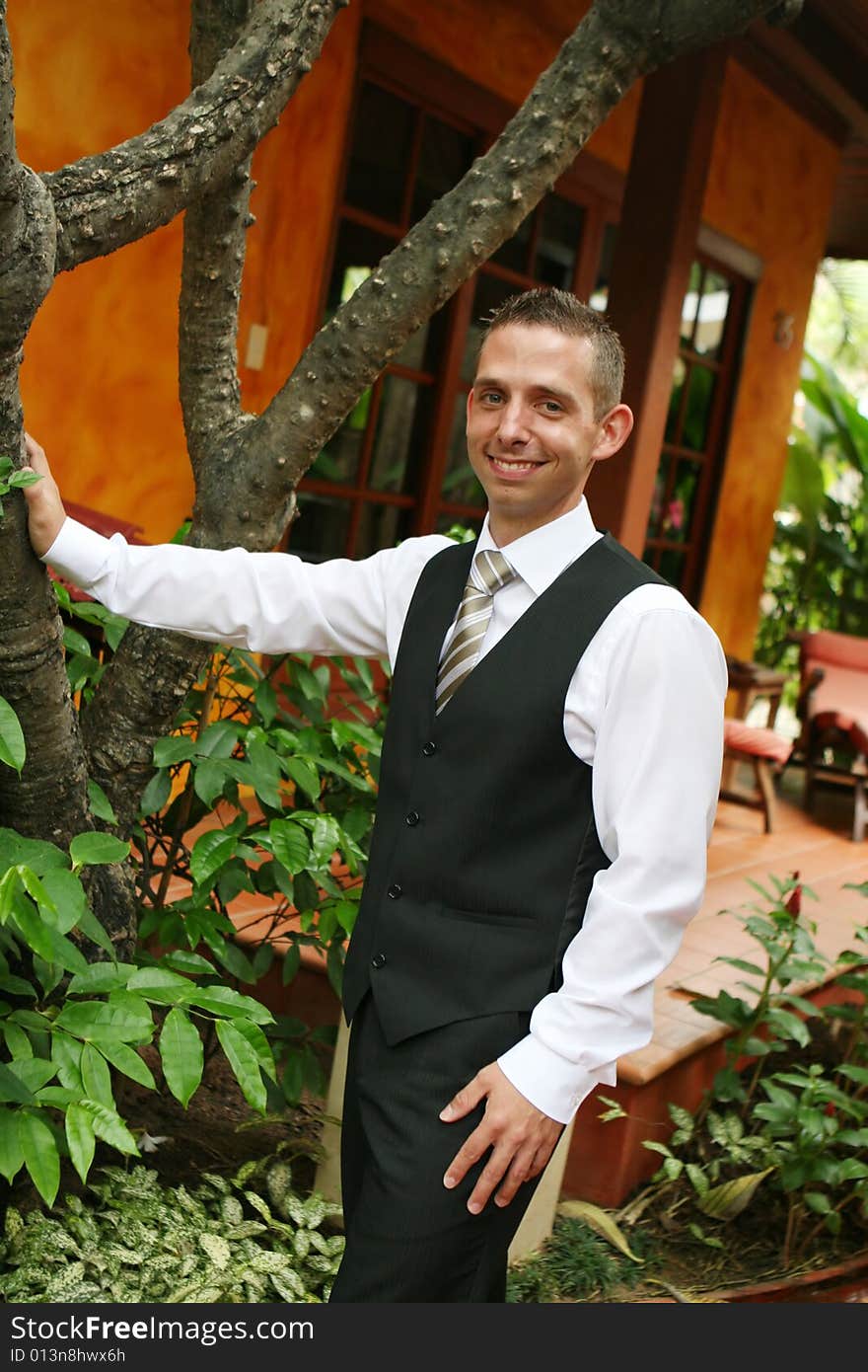 Happy young groom leaning on a tree.