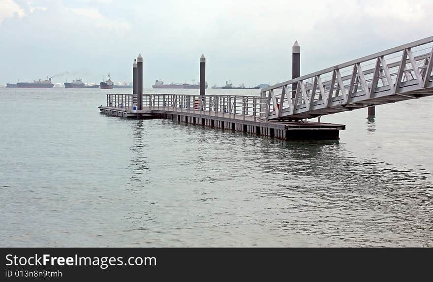 A floating pier linked by a suspended walkway against a busy shipping horizon