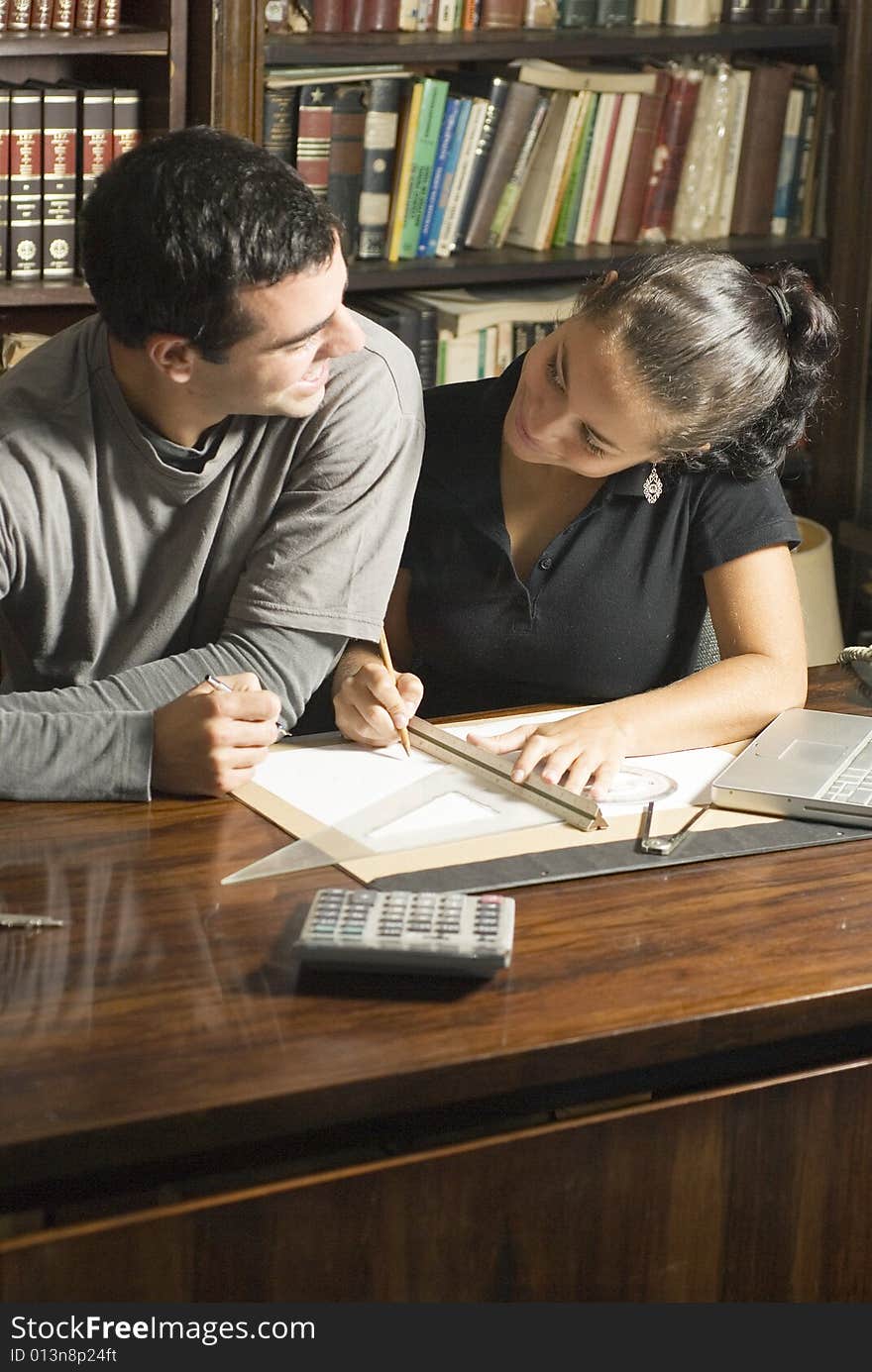 Two students smiling at each other as they work at a desk with a laptop, calculator, ruler, and calculator on it. Vertically framed photo. Two students smiling at each other as they work at a desk with a laptop, calculator, ruler, and calculator on it. Vertically framed photo.