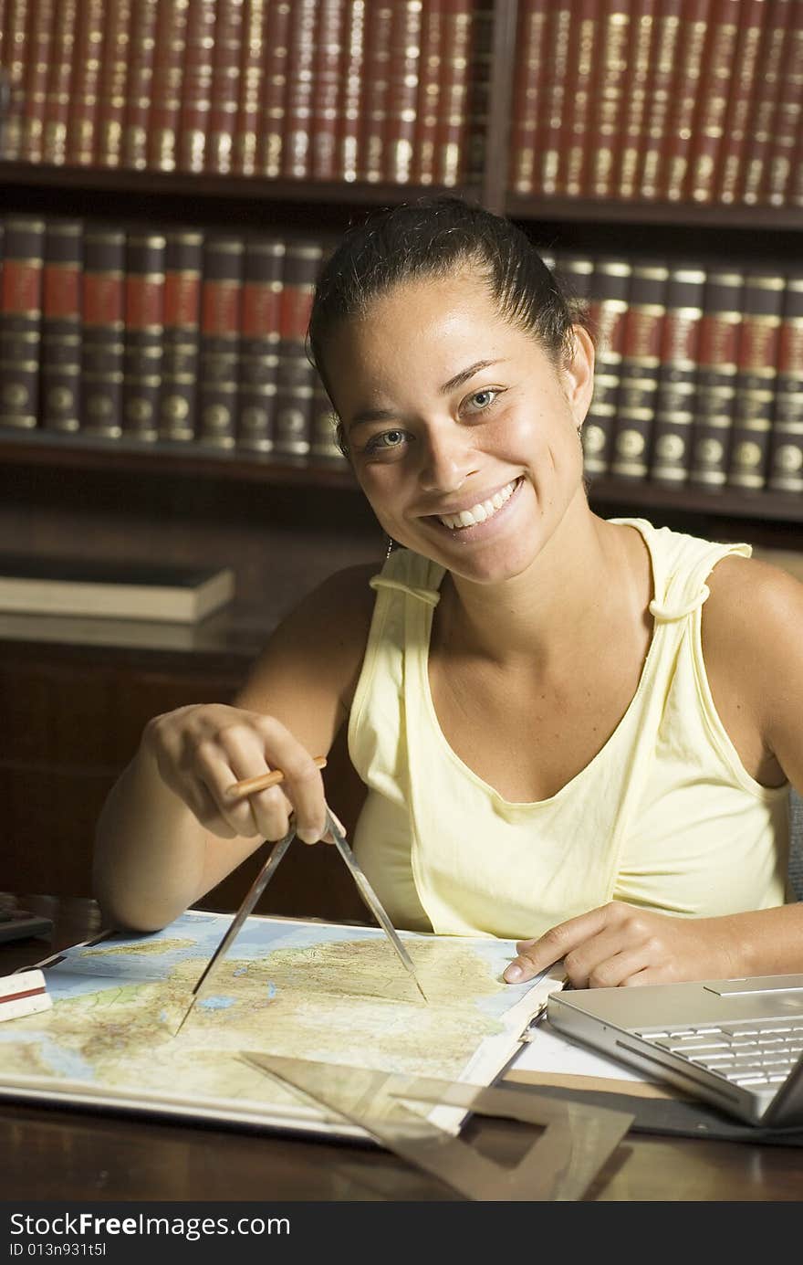 Smiling woman working at desk with a protractor, laptop, and ruler with books in the background. Vertically framed photo. Smiling woman working at desk with a protractor, laptop, and ruler with books in the background. Vertically framed photo.