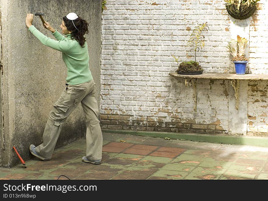 Woman hammers nail into wall. She is wearing a dust mask on her head. Horizontally framed photo. Woman hammers nail into wall. She is wearing a dust mask on her head. Horizontally framed photo.