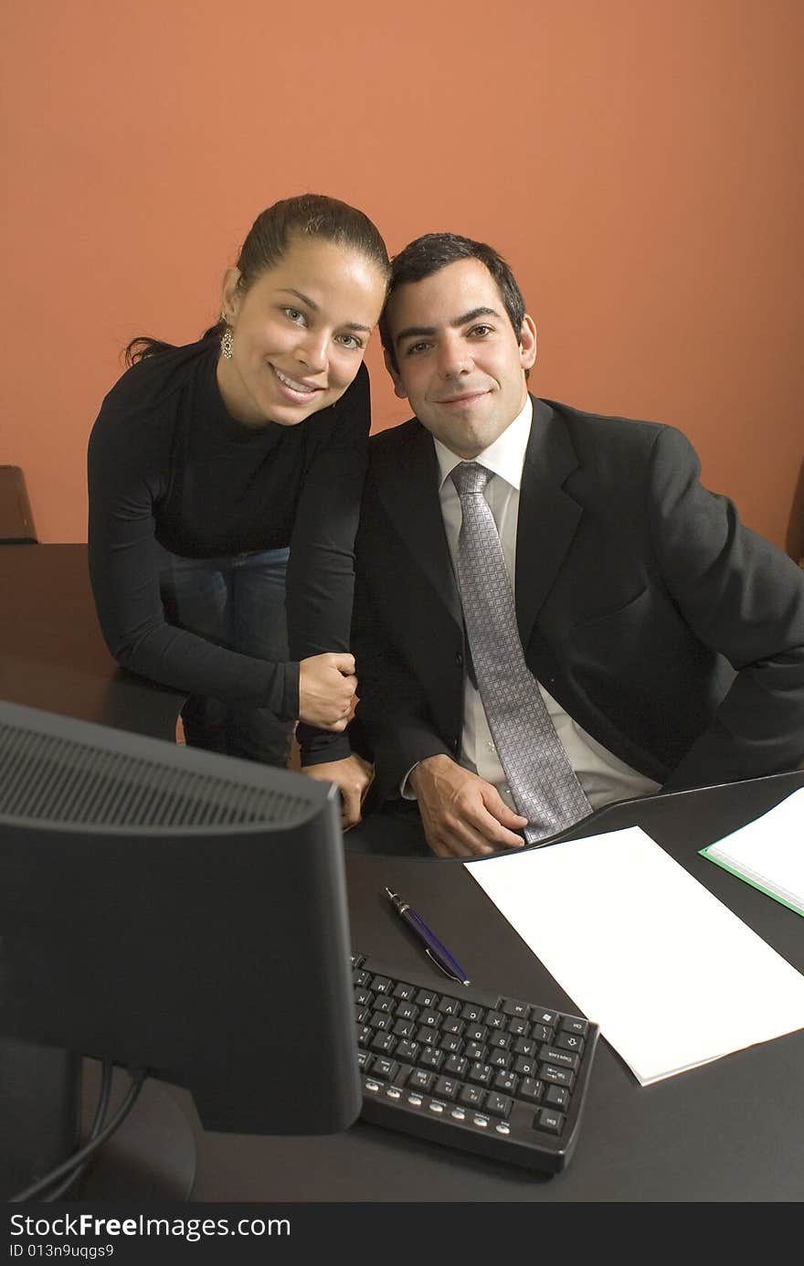 Businessman and woman smile with their heads touching as they work at a desk with a computer. Vertically framed photograph. Businessman and woman smile with their heads touching as they work at a desk with a computer. Vertically framed photograph.