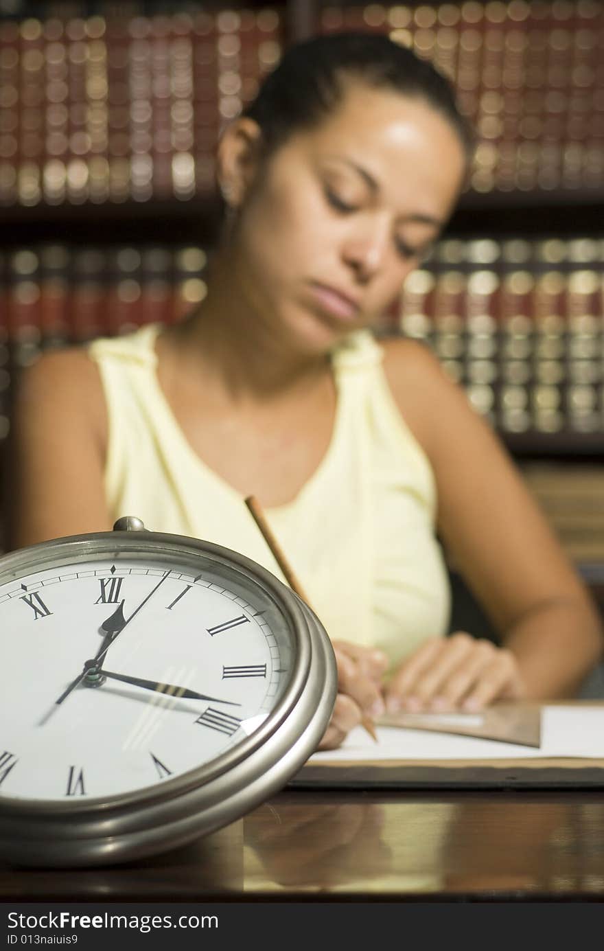 Girl in office with books writing at desk beside a clock. Horizontally framed photo. Girl in office with books writing at desk beside a clock. Horizontally framed photo.