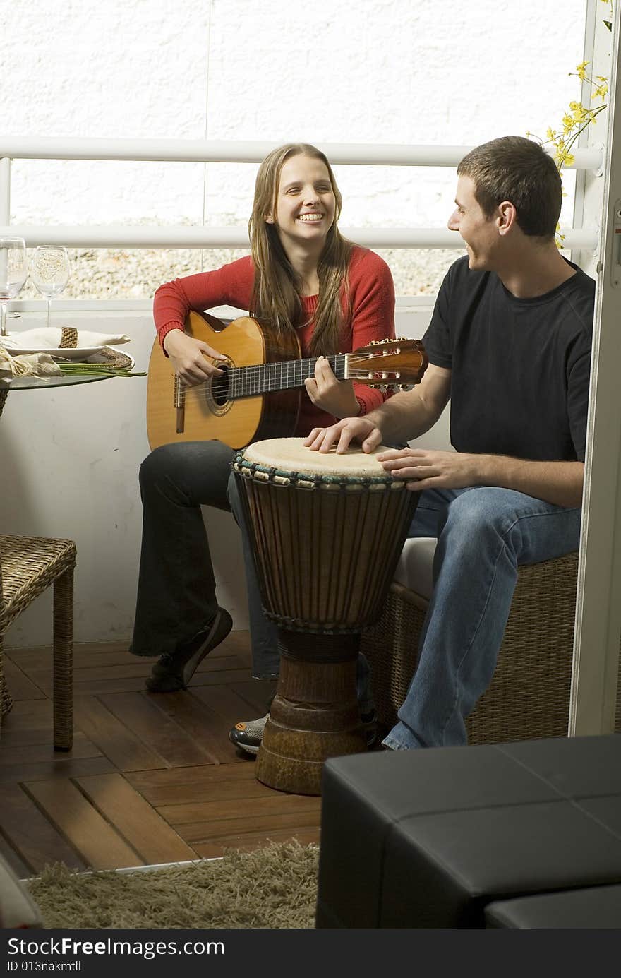 Woman playing guitar as she smiles at the man next to her on the drums. Vertically framed photo. Woman playing guitar as she smiles at the man next to her on the drums. Vertically framed photo.