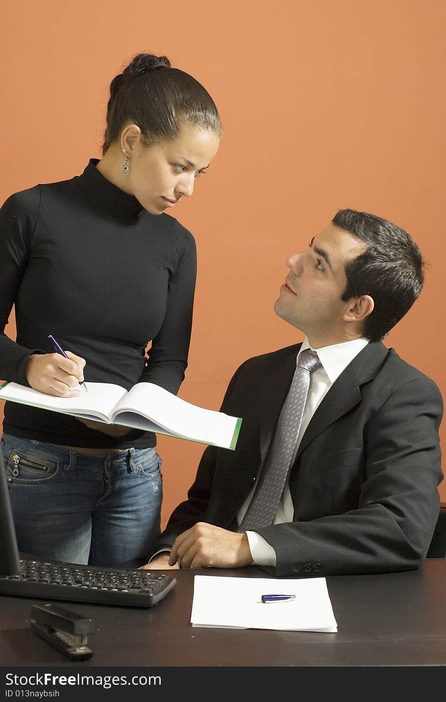 Woman takes notes for a business man sitting at a desk. Vertically framed photo. Woman takes notes for a business man sitting at a desk. Vertically framed photo.