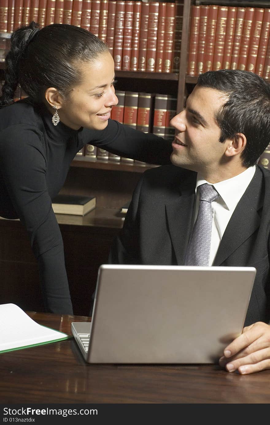 Businessman and woman smiling at each other surrounded by books and a laptop. Vertically framed photo. Businessman and woman smiling at each other surrounded by books and a laptop. Vertically framed photo.