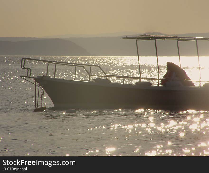 Boat silhouette in the sunset, sunrays glitter on the water, island in the background. Boat silhouette in the sunset, sunrays glitter on the water, island in the background