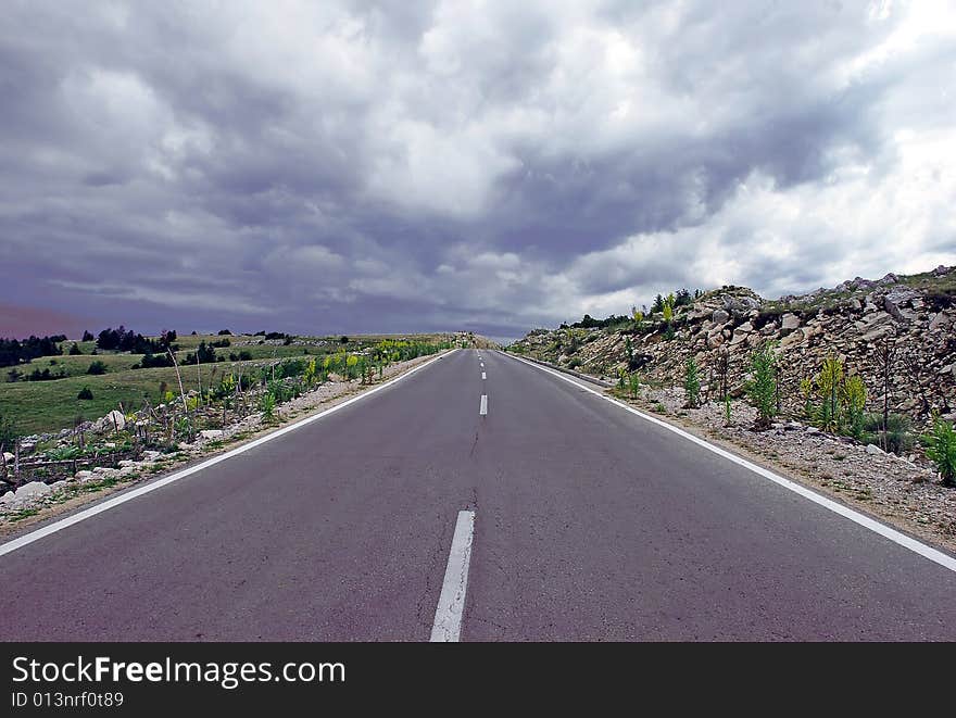 Gray road through mountain landscape under cloudy sky. Gray road through mountain landscape under cloudy sky