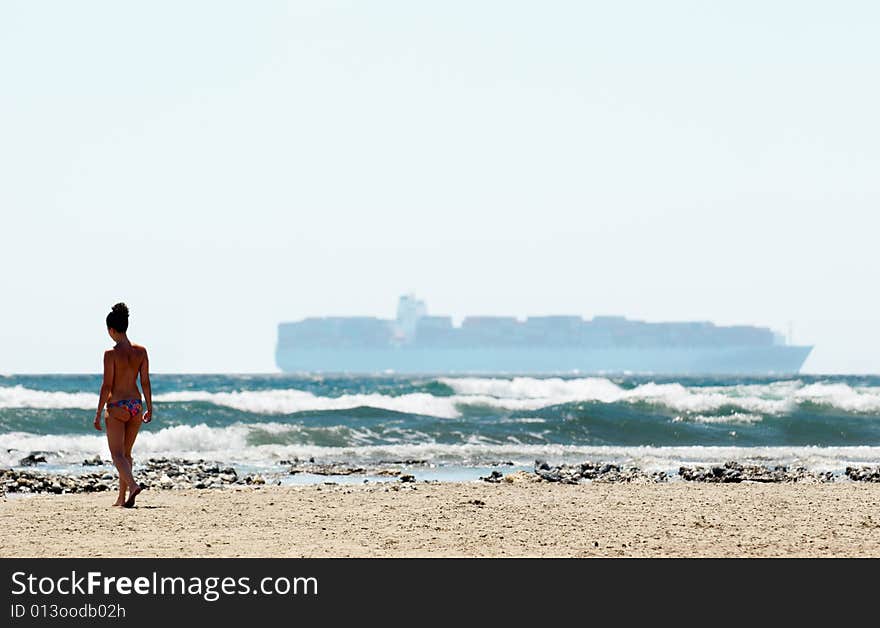 Woman going along the beach against big ship on the horizon of the sea. Woman going along the beach against big ship on the horizon of the sea