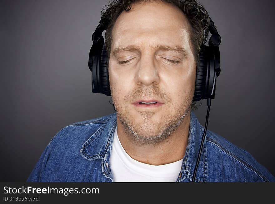 Man with Eyes Shut Wearing Headphones Enjoying His Music on a Grey Background. Man with Eyes Shut Wearing Headphones Enjoying His Music on a Grey Background.