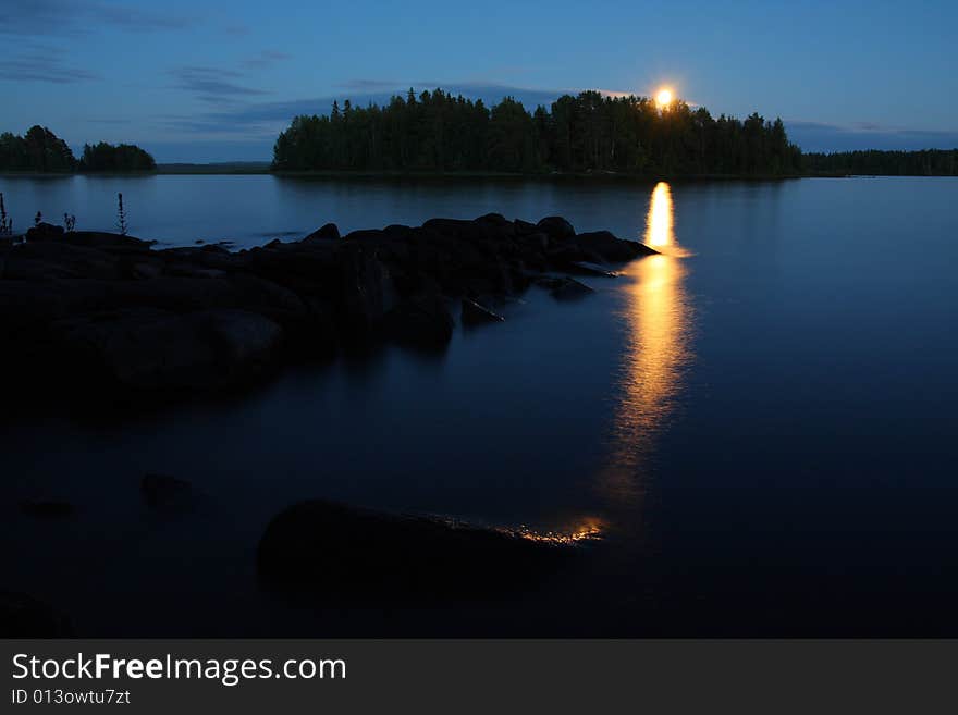 Moon rising and reflecting in the still water of a lake