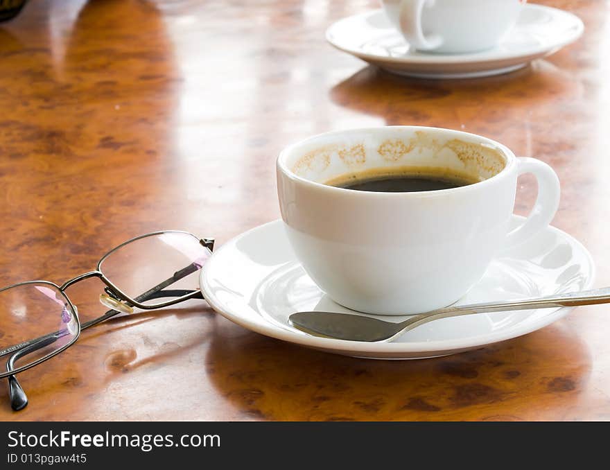 Two cups of partly drank coffee, and a pair of spectacles, on a marbled table top in the afternoon. Two cups of partly drank coffee, and a pair of spectacles, on a marbled table top in the afternoon