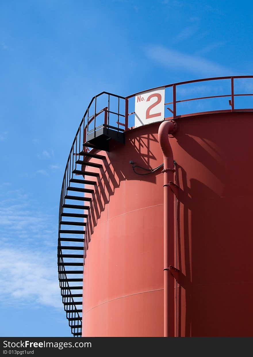 Red colored tank with a spiral staircase to its roof in a blue sky. Red colored tank with a spiral staircase to its roof in a blue sky