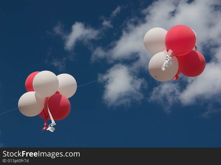 Red and white balloons with ribbons against blue sky.