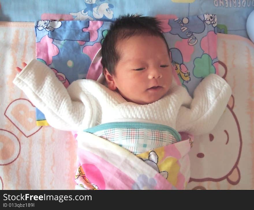 A Chinese baby is waving her hand on a bed. A Chinese baby is waving her hand on a bed