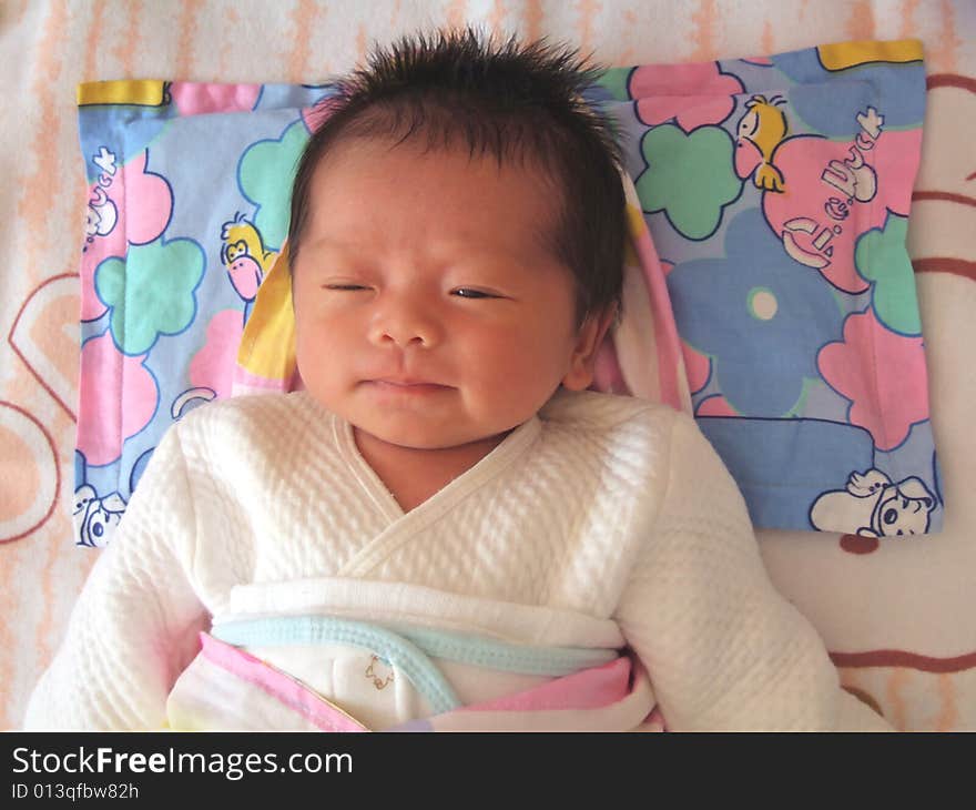 A Chinese infant is smiling on a bed. A Chinese infant is smiling on a bed