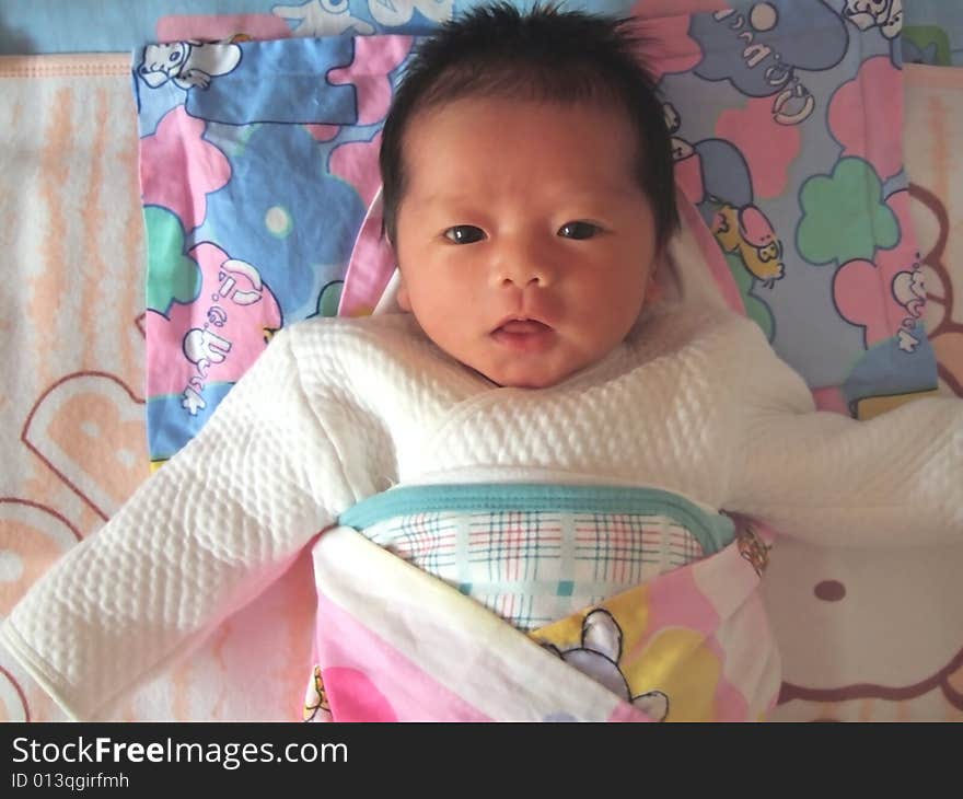 A Chinese infant is waving her hand on the bed. A Chinese infant is waving her hand on the bed