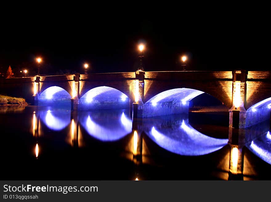 An old stone and brick bridge lit up by modern lights at night, old and new together. An old stone and brick bridge lit up by modern lights at night, old and new together.