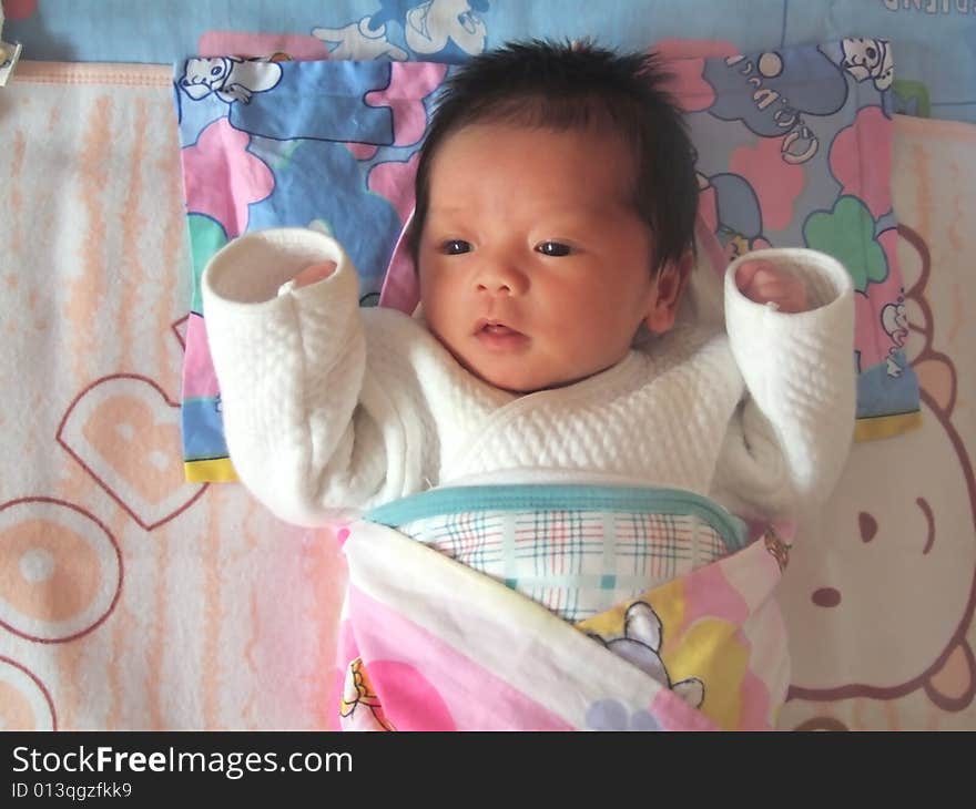 A Chinese infant is waving her hand on the bed. A Chinese infant is waving her hand on the bed