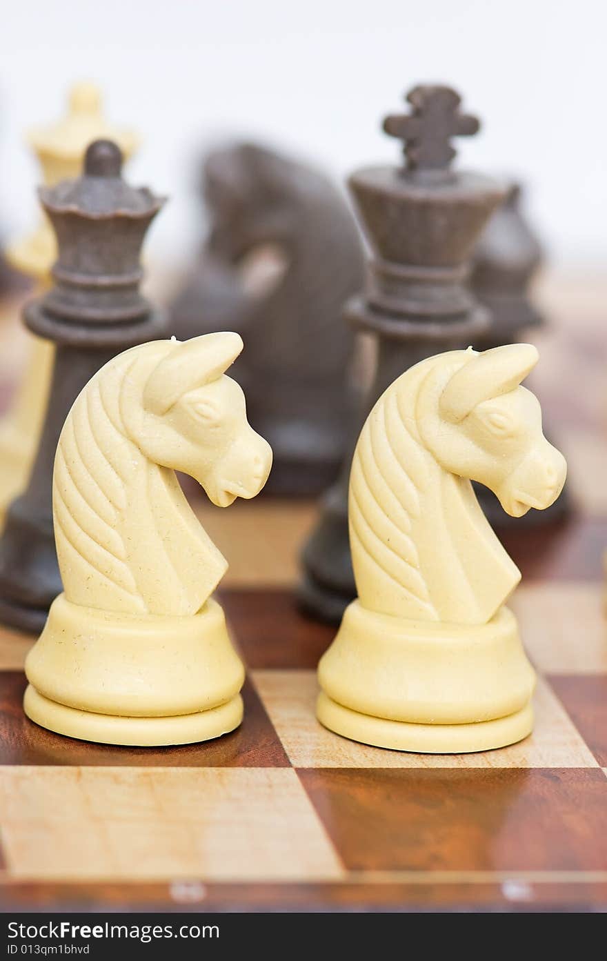 Macro of a chess board with a few chess pieces and other chess pieces like black king blurred in the background. This photo can be used to depict teamwork, diversity, power, leadership etc. Macro of a chess board with a few chess pieces and other chess pieces like black king blurred in the background. This photo can be used to depict teamwork, diversity, power, leadership etc