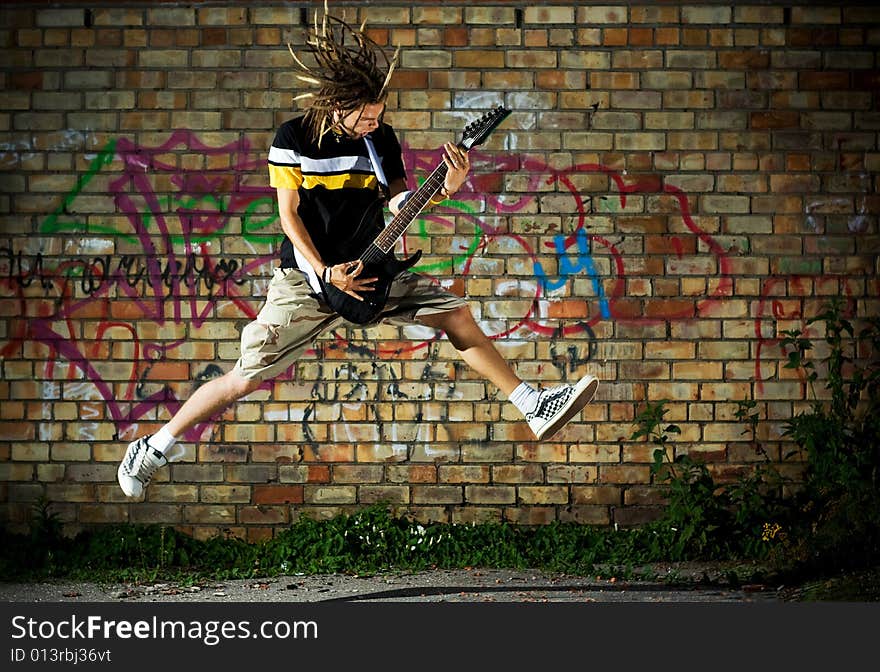 Young man with guitar jumping against the wall. Young man with guitar jumping against the wall.