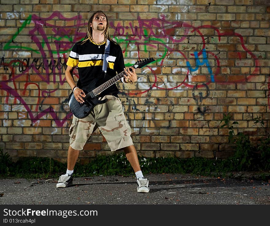 Young man standing with guitar against the wall. Young man standing with guitar against the wall.