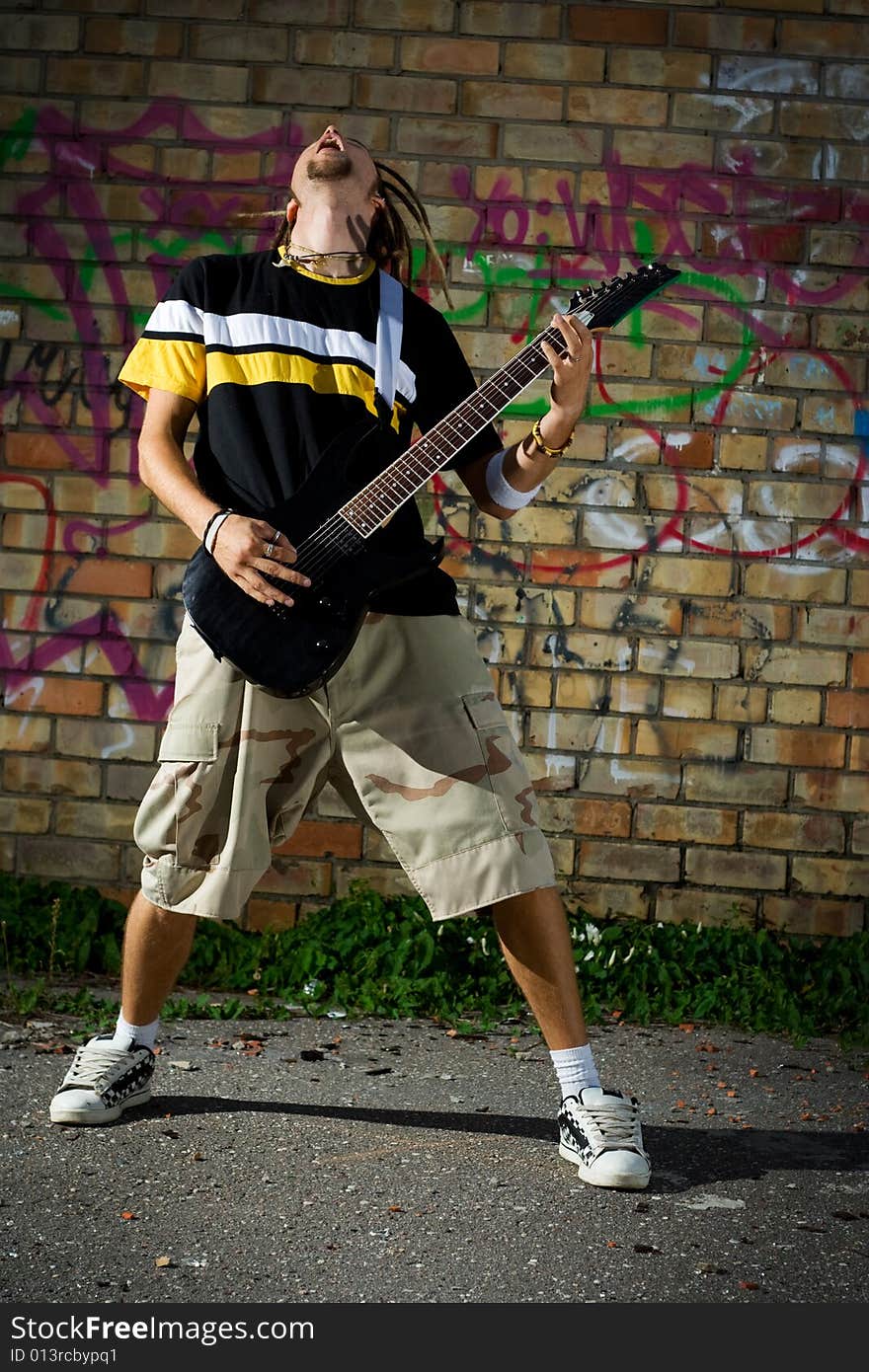 Young man playing the guitar and singing against the wall. Young man playing the guitar and singing against the wall.