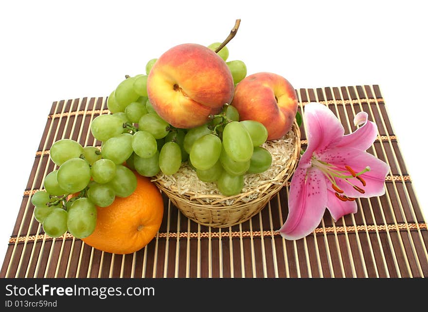 Beautiful flower of a lily and fruit in a yellow basket on a striped brown napkin on a white background. Beautiful flower of a lily and fruit in a yellow basket on a striped brown napkin on a white background