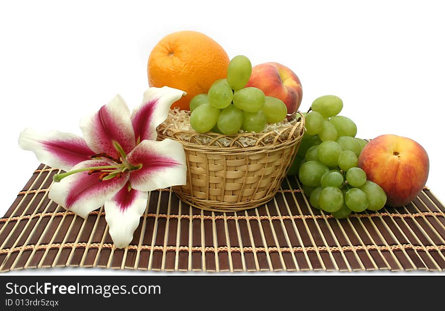 Beautiful flower of a lily and fruit in a yellow basket on a striped brown napkin on a white background