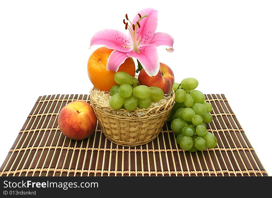 Beautiful flower of a lily and fruit in a yellow basket on a striped brown napkin on a white background